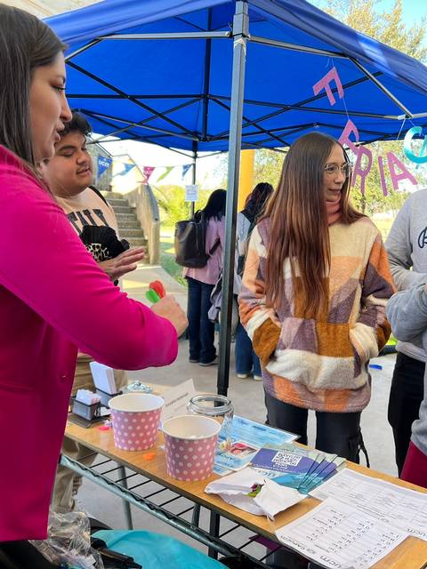 Un grupo de jóvenes interactúa en un puesto de feria mientras una mujer les habla.