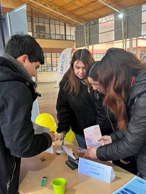 Un grupo de cuatro personas interactuando en un evento, con actividades en una mesa, dentro de un espacio cerrado.