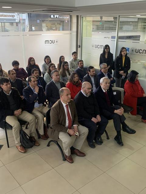 Un grupo de personas sentadas en un salón con un ambiente de reunión formal.