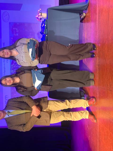 Tres personas en un evento académicamente formal, sosteniendo reconocimientos.