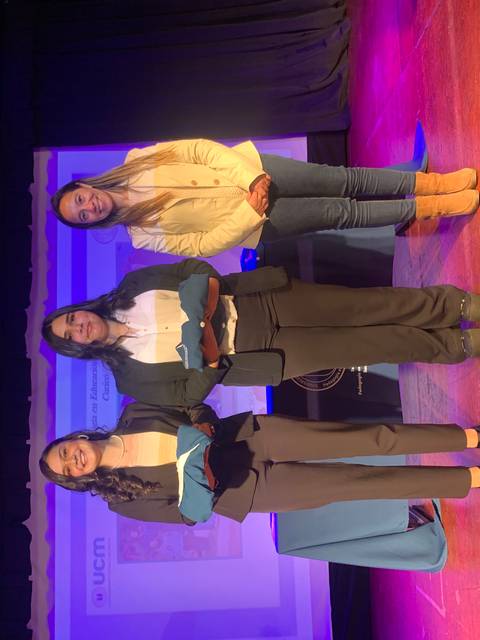 Tres mujeres posan juntas en un escenario durante un evento.