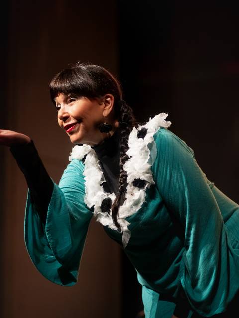 Una mujer sonriente se presenta en el escenario con un vestido colorido y un gesto acogedor.