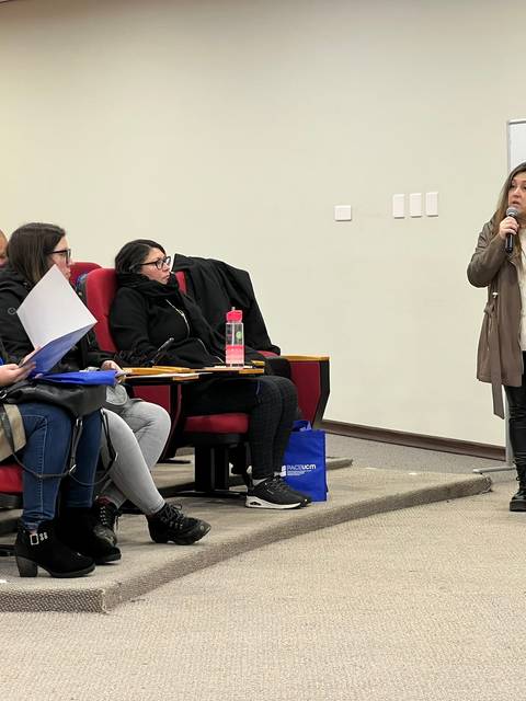 Una mujer presenta mientras un grupo de personas la escucha atentamente en un auditorio.