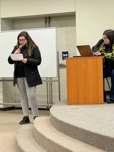 Una joven está hablando en un micrófono mientras otra mujer escucha desde una mesa.