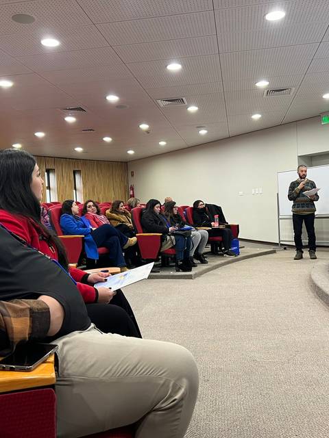Una sala de conferencias donde varias personas están sentadas escuchando a un orador frente a ellos.