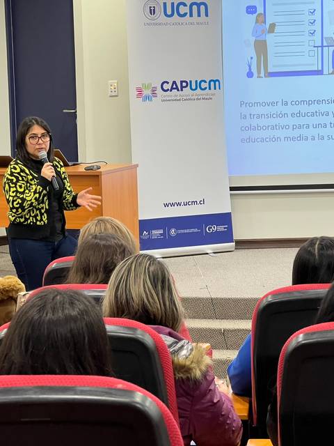 Una presentadora habla frente a un grupo de personas en una sala de conferencias.