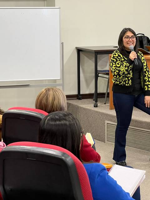 Una mujer habla y se presenta a un grupo deAudience en una sala de clases.