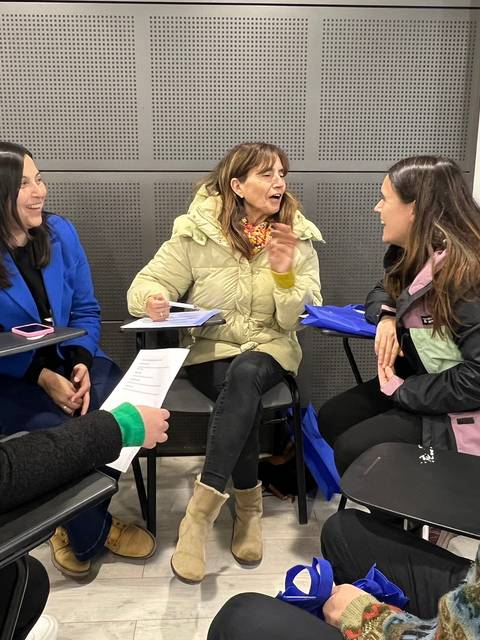 Un grupo de seis personas está conversando animadamente sentadas alrededor de una mesa.