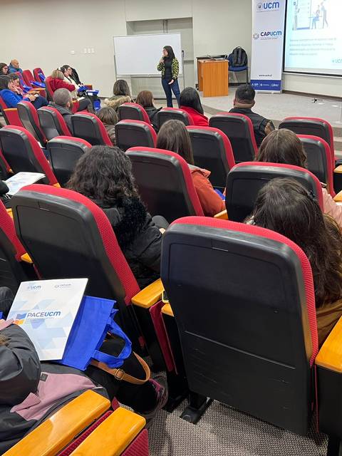 Una presentación en un aula con varias personas sentadas en sillas rojas.