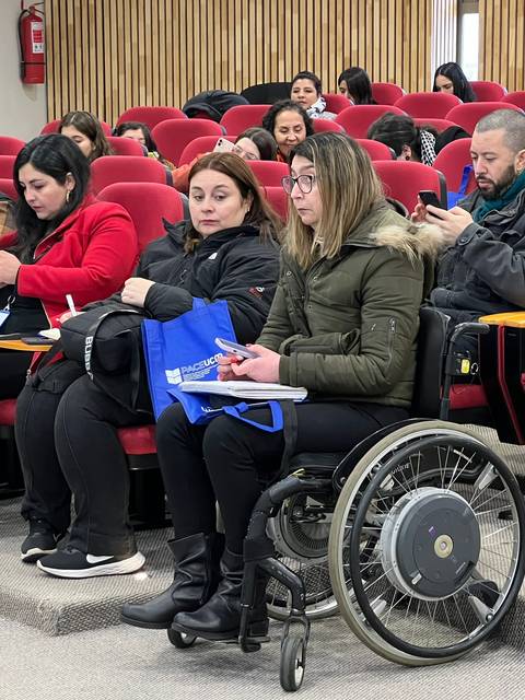Un grupo de personas sentadas en un auditorio, prestando atención a sus dispositivos móviles.