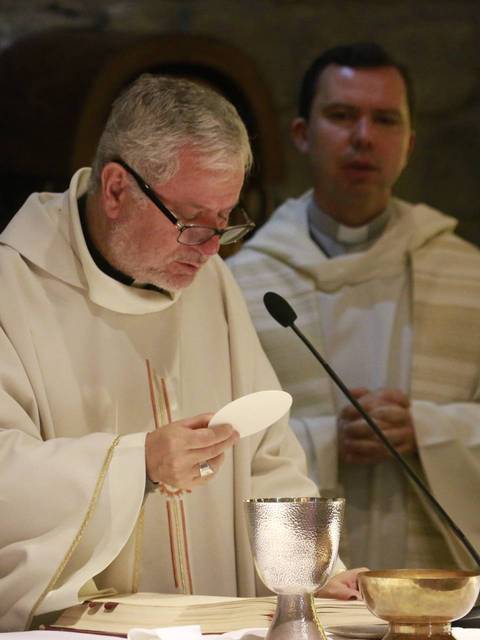 Un sacerdote celebra una misa sosteniendo la hostia frente a él.