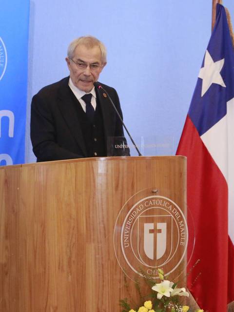 Un hombre de pie, detrás de un podio, habla en un evento en una universidad chilena.
