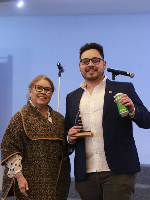 Una mujer y un hombre posan juntos en un evento, mostrando un reconocimiento.