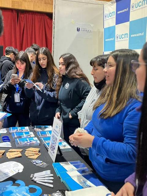 Un grupo de personas en un stand de información con material promocional sobre una institución educativa.