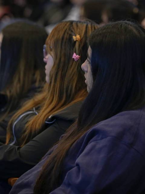 Grupo de jóvenes sentadas en una sala, prestando atención a un evento.