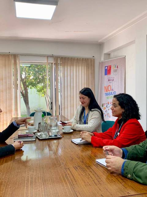 Cuatro personas se reúnen en una mesa de oficina, conversando en un ambiente profesional.