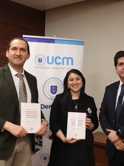 Un grupo de tres personas sonríen mientras sostienen libros en una ceremonia en la UCM.