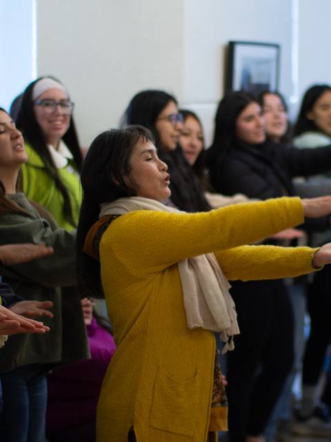 Un grupo de mujeres participa en una actividad organizada, expresándose con las manos en un ambiente iluminado.