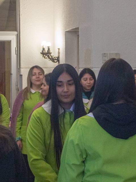 Un grupo de mujeres se reúne en un espacio cerrado, varias de ellas visten chaquetas verdes y se observan interacciones entre ellas.
