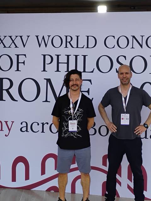 Dos personas posan frente a un fondo que anuncia el XXV Congreso Mundial de Filosofía en Roma 2024.