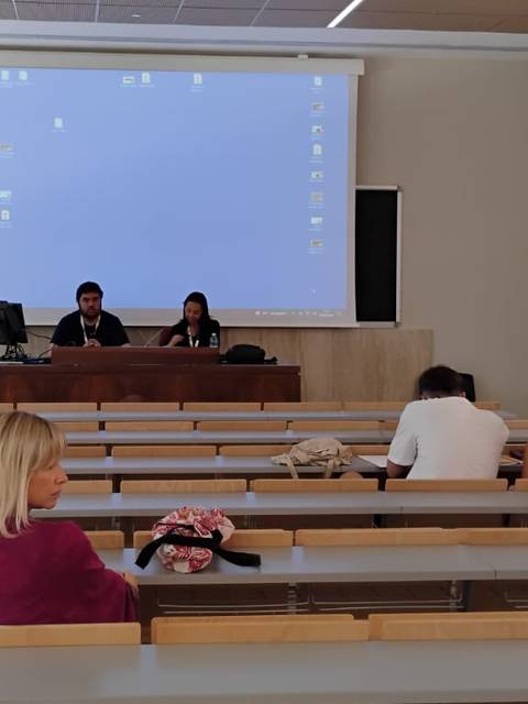Una sala de conferencias con un grupo de personas sentadas y dos presentadores en el frente.