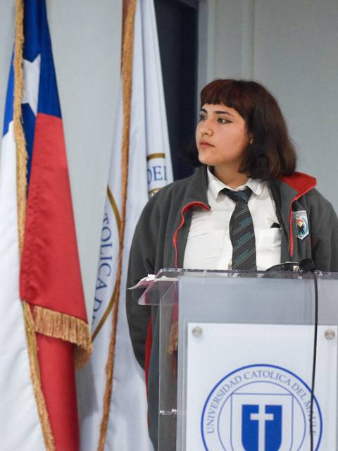 Una joven se encuentra de pie junto a una bandera, mientras observa en dirección opuesta a la cámara.