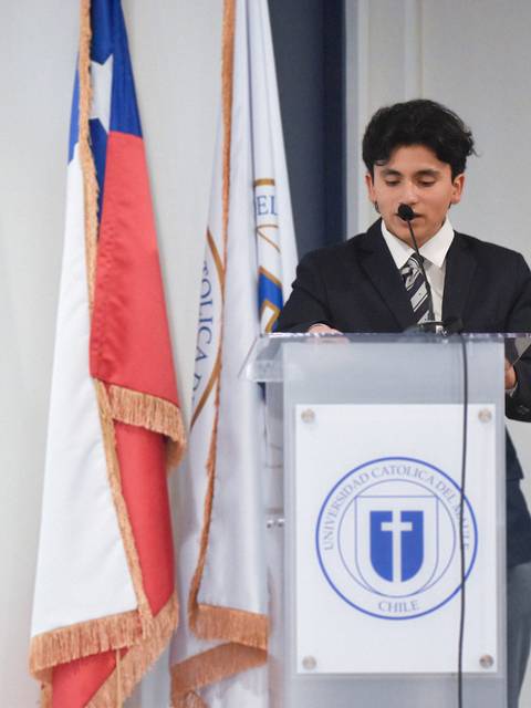Un joven está hablando en un podio frente a banderas chilenas y una insignia de una institución educacional.