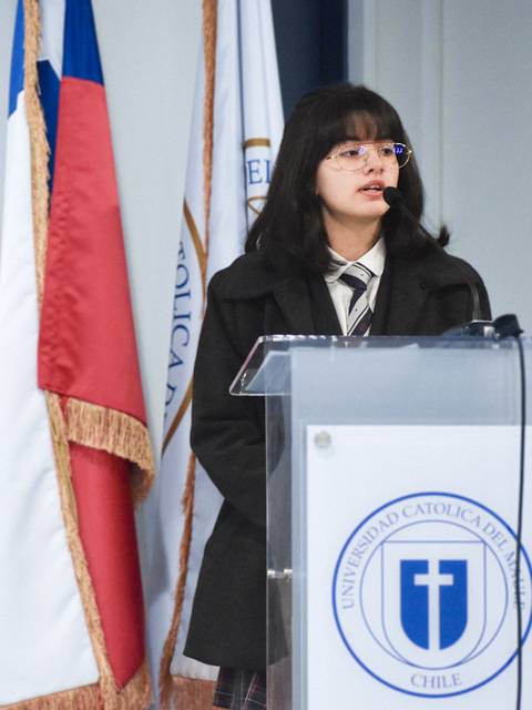 Una joven habla en un podio frente a banderas de Chile y de una universidad.