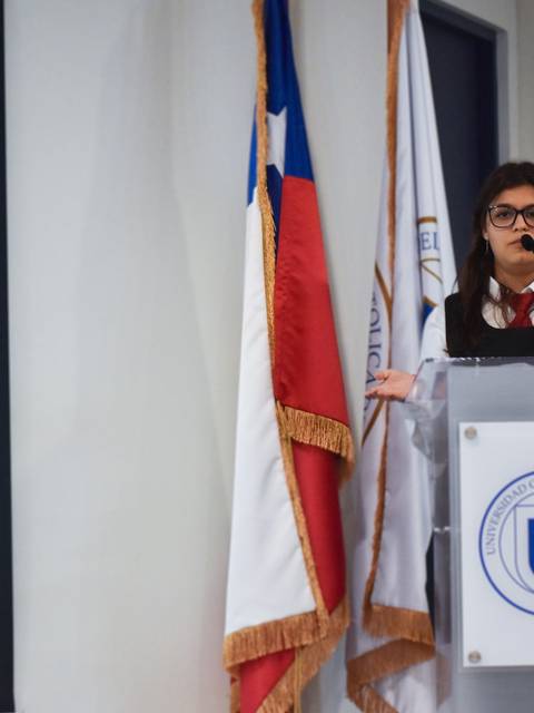 Una persona está presentando en un escenario con banderas de Chile y una proyector detrás.