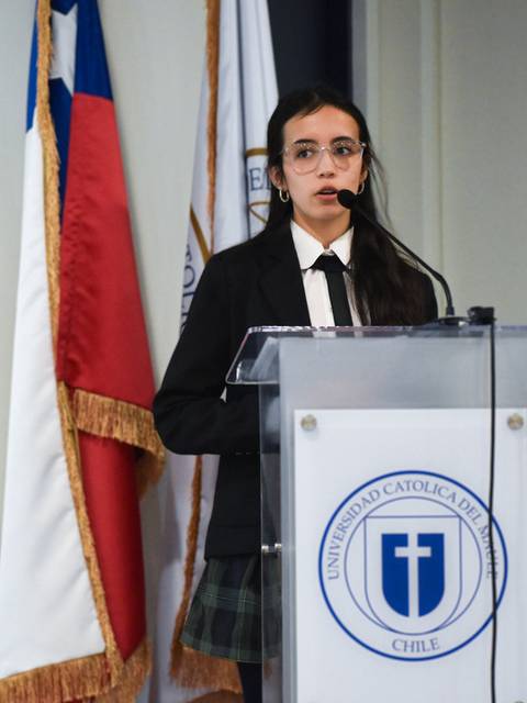 Una joven que se encuentra hablando en un atril frente a una bandera chilena.