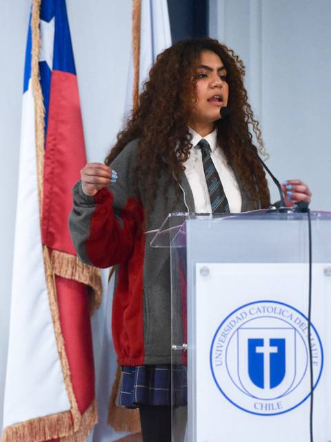 Una joven habla en un podio con una bandera chilena en el fondo.
