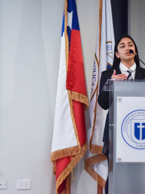 Una joven está hablando frente a un público en un auditorio, con una presentación proyectada detrás de ella.