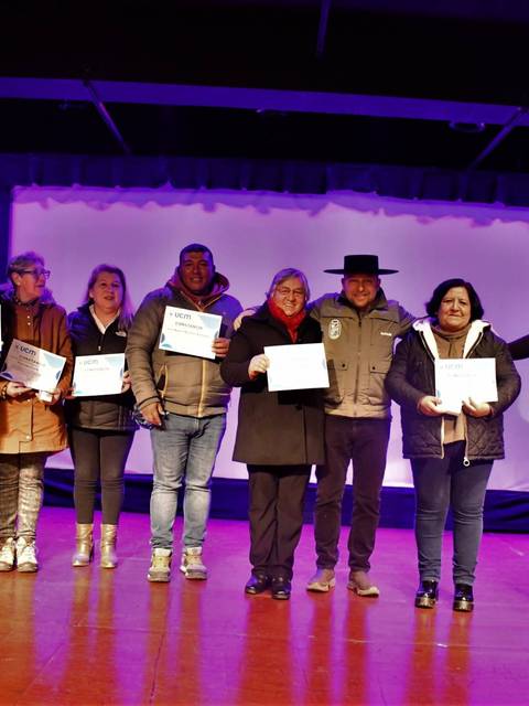 Un grupo de personas posando en un escenario sosteniendo certificados durante un evento.