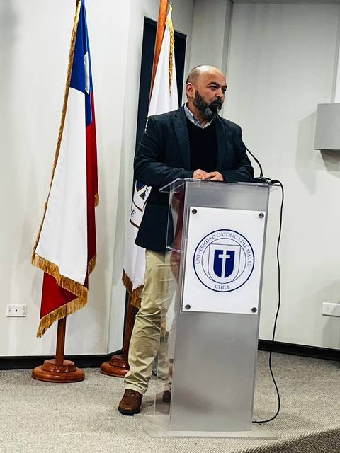 Un hombre habla desde un podio en un evento oficial con banderas de fondo.
