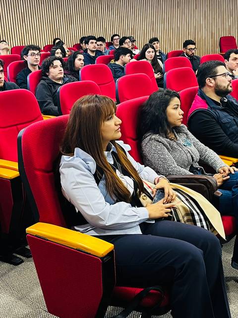 Un grupo de personas sentadas en un auditorio con sillas rojas durante un evento o presentación.