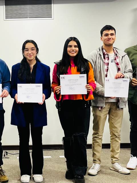 Un grupo de seis personas sonríen mientras sostienen certificados en un evento de entrega de reconocimientos.