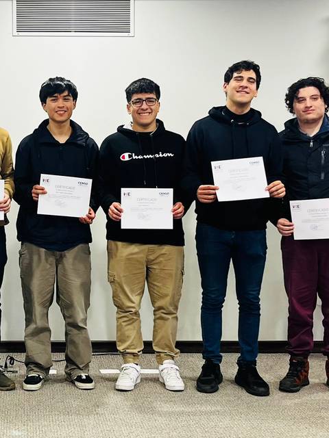 Un grupo de seis personas, incluidas cinco jóvenes y un hombre mayor, posan con certificados en manos en un evento de entrega de premios.