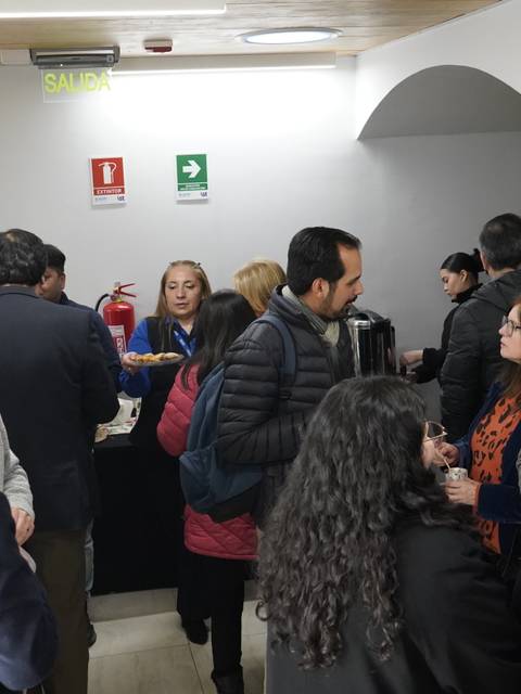 Un grupo de personas conversando en un pasillo con bebidas y arte en las paredes.