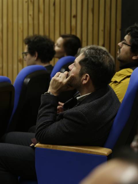 Un grupo de personas asiste a una conferencia en un auditorio con asientos azules.