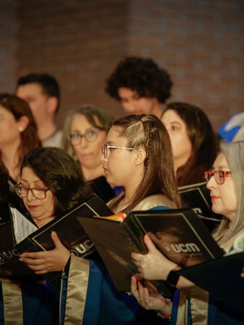 Un grupo de personas cantando en un coro con vestimenta formal y partituras en mano.