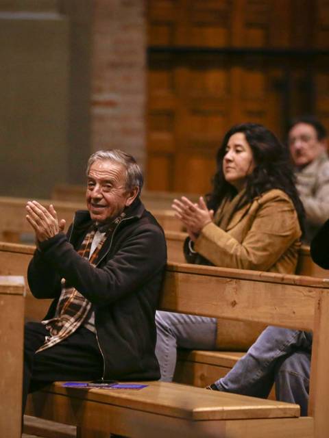 Un grupo de personas aplaudiendo sentadas en un banco de madera en un entorno interior.