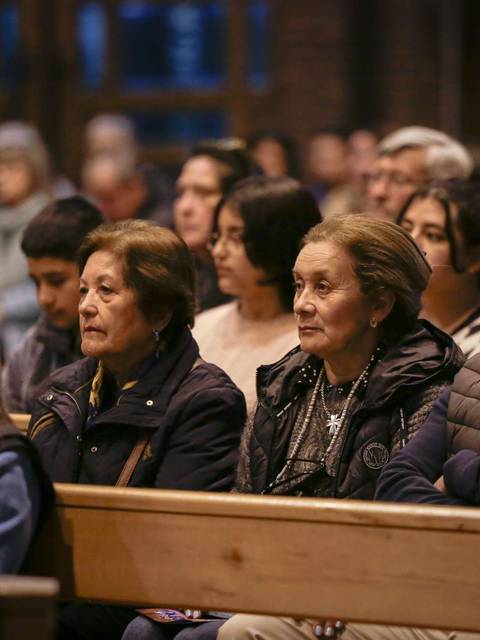 Un grupo de personas sentadas en un banco en un ambiente interior, mirando hacia adelante.