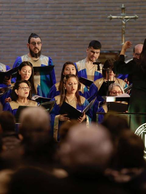 Un coro de personas cantando bajo la dirección de un/a director/a en un evento religioso.
