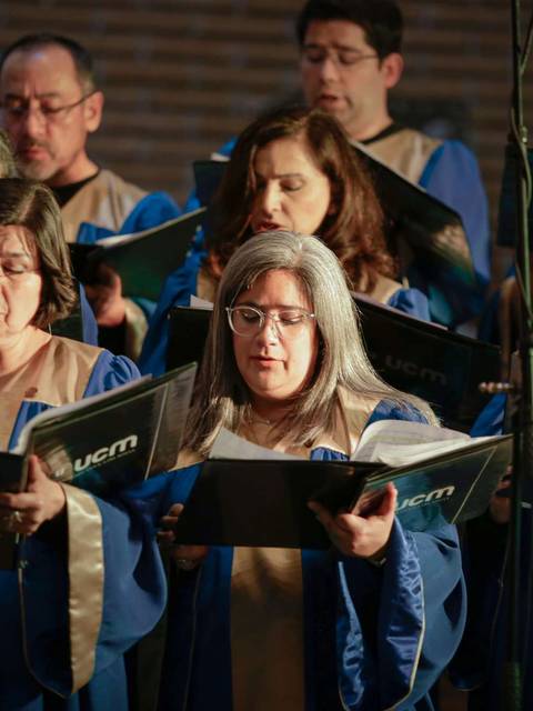 Un grupo de personas cantando en un coro mientras sostienen partituras.