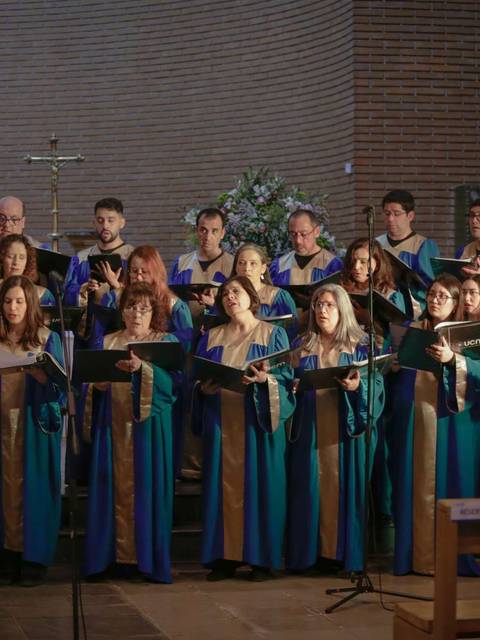 Un coro vestido con túnicas azules y doradas canta durante una actuación en un interior con bancos de madera.