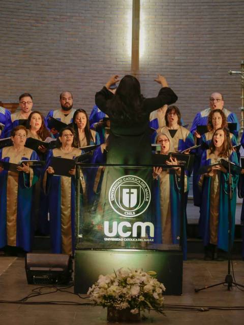 Un coro de personas cantando bajo la dirección de un director en un ambiente solemne.