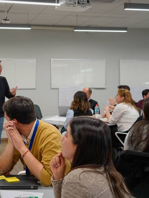 Un grupo de personas en una sala de clases donde un presentador está hablando frente a ellos.