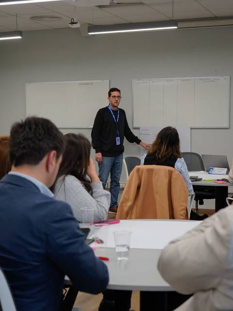 Un hombre está presentando en una sala de conferencias mientras un grupo de personas lo observa atentamente.