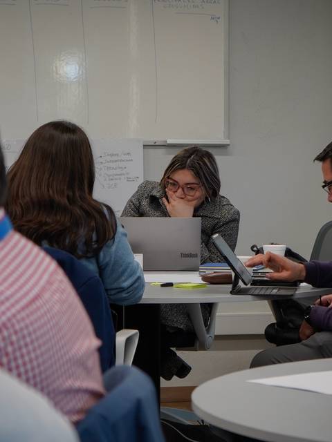 Un grupo de personas en una reunión, concentradas en sus laptops y tomando apuntes.