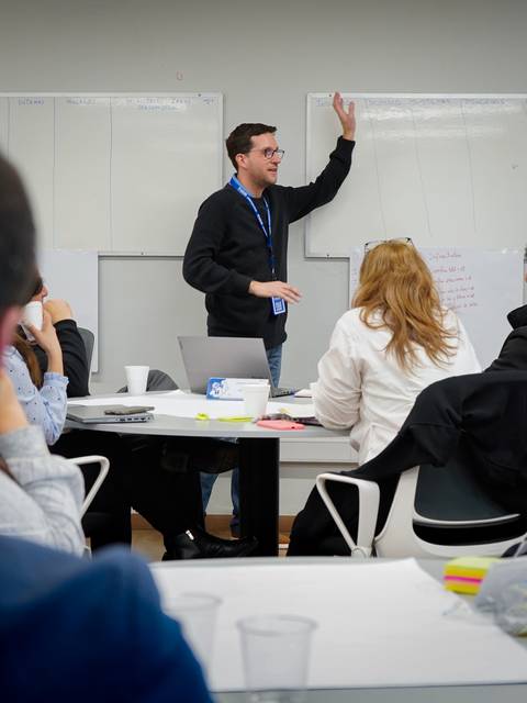 Un hombre presenta en una sala de reuniones mientras otros participantes lo observan.